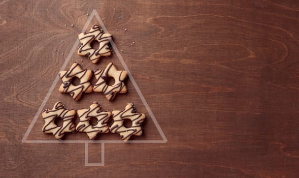 Christmas tree form made from star-shaped cookies with chocolate, banner on the brown wooden background with copy space