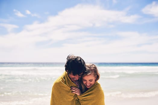 Staying warm together. an affectionate young couple wrapped in a blanket on the beach.