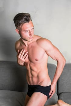 Photo of a shirtless man sitting on a couch in black underwear
