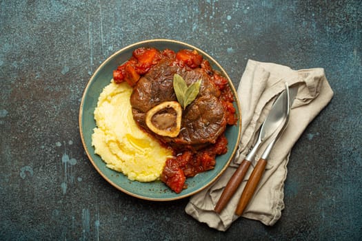 Traditional Italian dish Ossobuco all Milanese made with cut veal shank meat with vegetable tomato sauce served with corn polenta on ceramic plate top view on rustic stone background