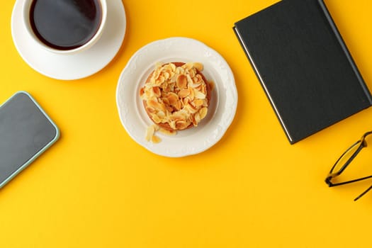 Tartlet with almond petals and cup of coffee on yellow background
