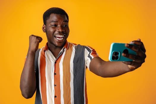 Young african man using smartphone againast yellow background