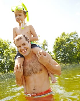 Playing in the lake with my son. Young father standing in a lake carrying his son on his shoulders and smiling.