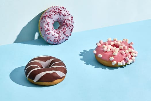 Three sweet tasty donuts in caramel and chocolate icing, on a two-color background