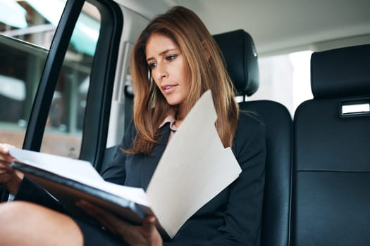 Getting work done on the go. a mature businesswoman going through paperwork in the back seat of a car.