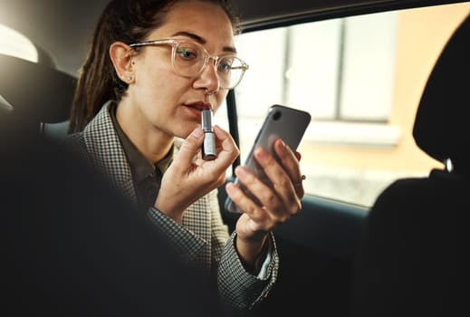 Phone, lipstick and a business woman in a car to travel in the city for work while multitasking. Face, mobile and makeup with a young female employee in a taxi or cab as a passenger for transport