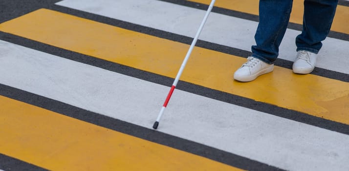 Close-up of the legs of a blind woman crossing the road at a crosswalk with a cane