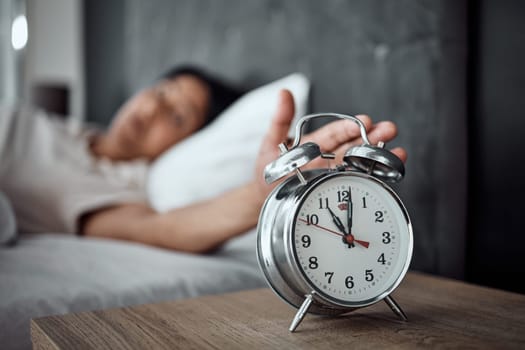 Alarm, sleeping and a hand with a clock for awake, oversleep or tired in the bedroom of a home. House, ring and a closeup of a person or woman in bed for snooze, rest or waking up lazy in a house
