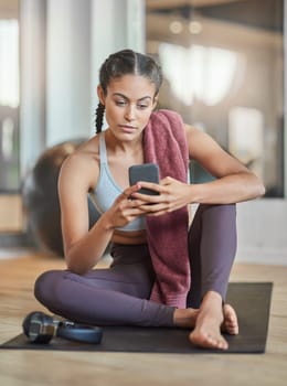 Checking her messages between sets. Full length shot of an attractive young female athlete checking her phone while sitting in the gym