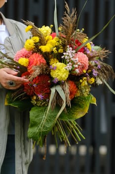 A large bouquet of mixed flowers in the hands of a woman. The work of a florist in a flower shop