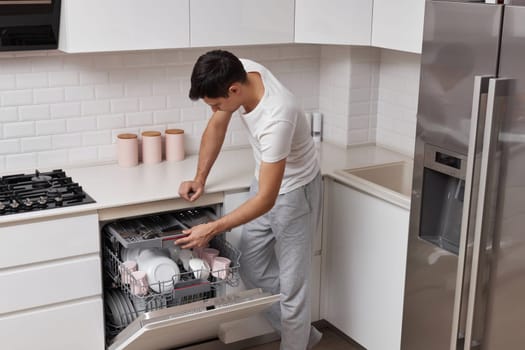 handsome positive man putting plates in dishwasher machine