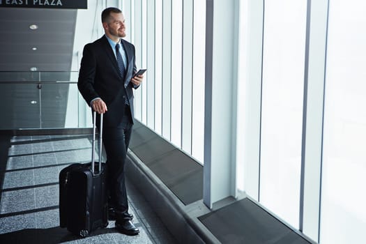 Business man, phone and airport window with suitcase for smile, thinking and idea for international travel. Entrepreneur, luggage and smartphone with flight schedule for global immigration in London