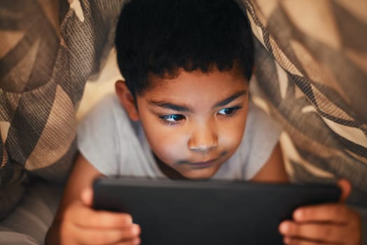 Hes too curious to sleep. an adorable little boy using a digital tablet while lying under a blanket at home.