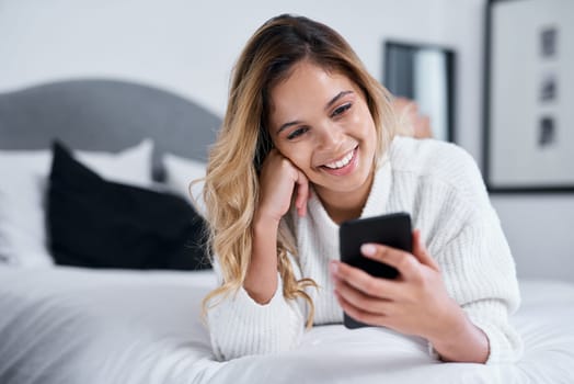 Theres so many fun things to keep you busy online. a young woman using her cellphone while lying on her bed.