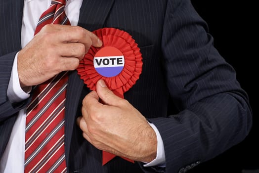 Man, vote and suit for election, ribbon and politician for support and on dark studio background. Politics, voter choice and representative for party, registration and democracy for voting register