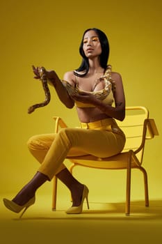 Just follow the yellow. a fashionable woman holding a snake while modelling a yellow concept.