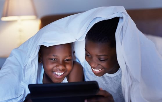 Time together as a family is a gift. a brother and sister using a tablet in bed at night.