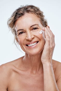 A good skincare routine is a must at any age. a mature woman posing with moisturiser on her face.