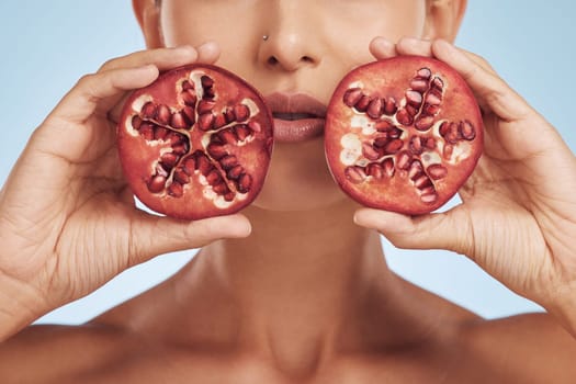 Hands, skincare and woman with pomegranate for beauty in studio isolated on a blue background. Natural, fruit and face of model with food for nutrition, healthy vegan diet and vitamin c for wellness.