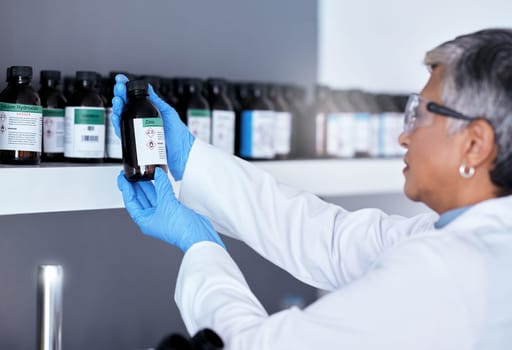 Laboratory, science and woman with bottle from shelf to check medical research information. Healthcare, medicine and innovation in manufacturing of vaccine or prescription drugs with senior scientist