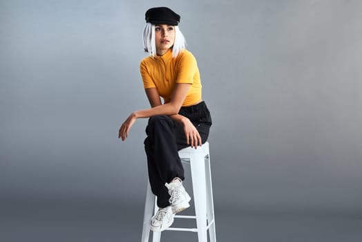 Do you know the history behind the baker boy hat. Studio shot of a beautiful young woman sitting on a stool against a grey background.