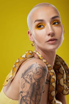 They should be scared of me. a young woman posing with a snake around her neck against a yellow background.