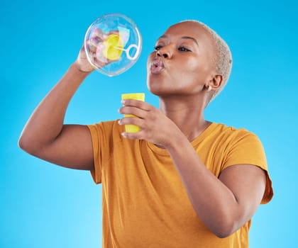 African, woman and blowing bubbles in studio, blue background or party celebration with fun, liquid soap or toy. Black model, person and relax with happy, joyful or creative play for enjoyment