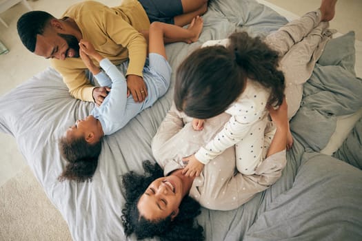 Happy family, from above and playing in bed in the morning, bond and having fun in their home together. Love, top view and children tickle parents in a bedroom, playful and relax in their house