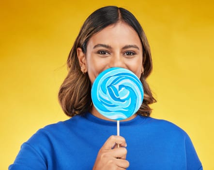 Lollipop, candy and portrait of woman with sweet dessert with sugar isolated in a studio yellow background with smile. Food, snack and young person with delicious treats, product or guilty pleasure