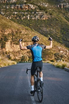 Man, cycling and celebration with back on mountain road, strong arm muscle or fist in air for winning. Winner athlete, bicycle or achievement for health, workout or training for performance in nature