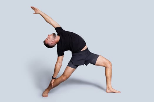 Calm young caucasian man with beard in sportswear practice yoga, stretching body