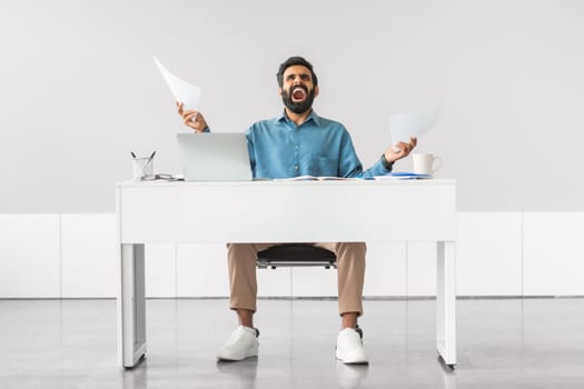 Stressed indian man with papers at office desk