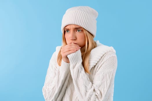 Woman in hat feeling cold, blue backdrop