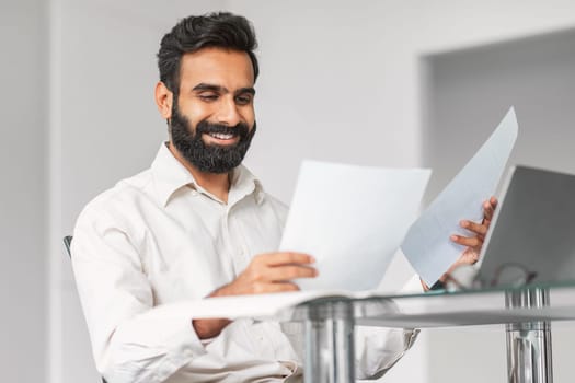 Smiling indian businessman reviewing papers at office desk