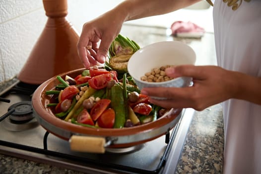 Close-up housewife's hands stacking fresh vegetables in a dishware from clay, preparing cooking tagine in the kitchen