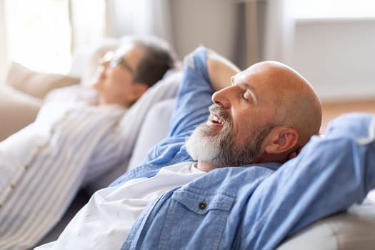 Happy Relaxed Senior Spouses Leaning Back On Comfortable Couch