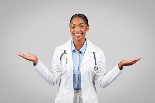 Cheerful millennial black lady doctor hold copy space on hands, spread arms