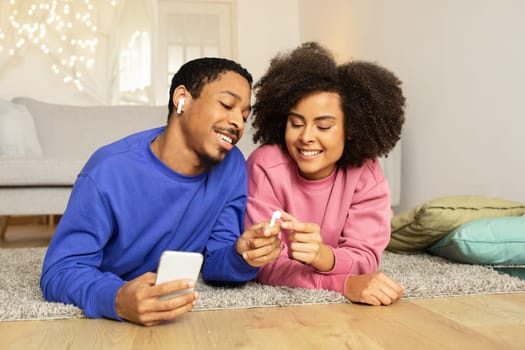 Black spouses enjoying online music via phone, sharing earphones indoor