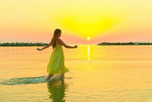 beautiful girl in a yellow dress running on the water at dawn.