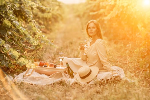 Woman picnic vineyard. Romantic dinner, fruit and wine. Happy woman with a glass of wine at a picnic in the vineyard on sunny day, wine tasting at sunset.