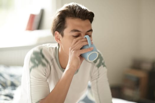 Relax, morning and a man drinking coffee in the bedroom of his home to relax or wake up on the weekend. Tea, caffeine or beverage with a young person on his bed in an apartment to enjoy a beverage