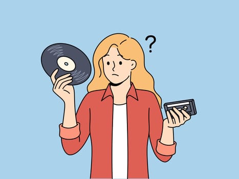 Girl with vinyl record and tape cassette looks confusedly at old-fashioned storage media with music