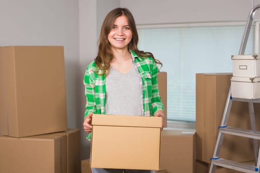 Portrait of woman carrying cardboard box in new house - Moving, new home and people concept