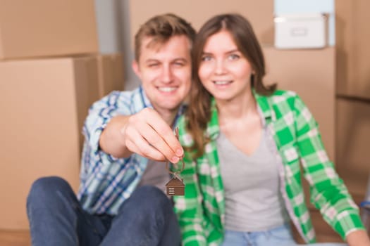 Happy young couple sitting on floor near boxes. Young family moving to new home. Woman and man showing keys and smiling at camera