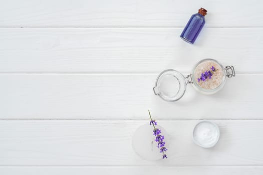 Herbal oil and lavender flowers on white wooden background
