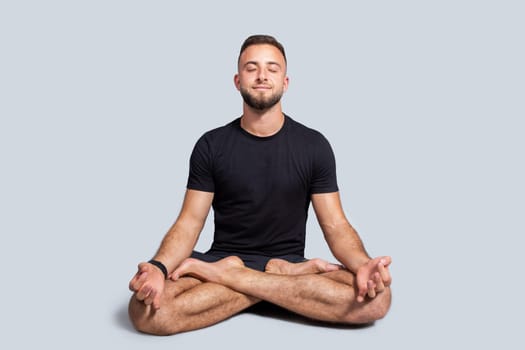 Positive millennial european man with beard in sportswear practice yoga in lotus position