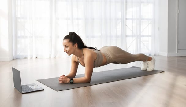 Young woman have workout at home, using laptop