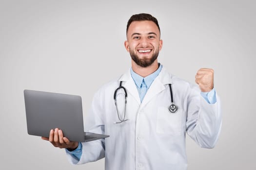 Happy man doctor with laptop and fist pump gesture