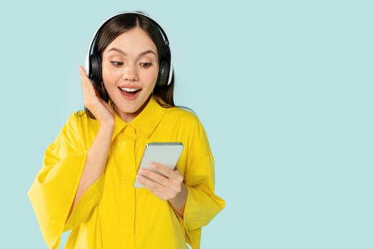 Amazed young woman enjoying music, using headphones and smartphone
