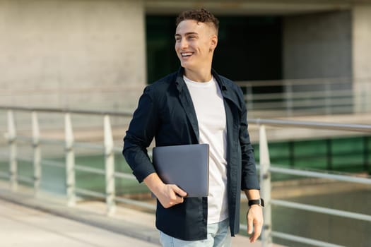 Cheerful confident attractive millennial caucasian man enjoy lifestyle, go with laptop in city
